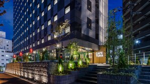 Un bâtiment moderne abritant un café appelé « CAFE TORA » au rez-de-chaussée, avec une terrasse et une façade en pierre.