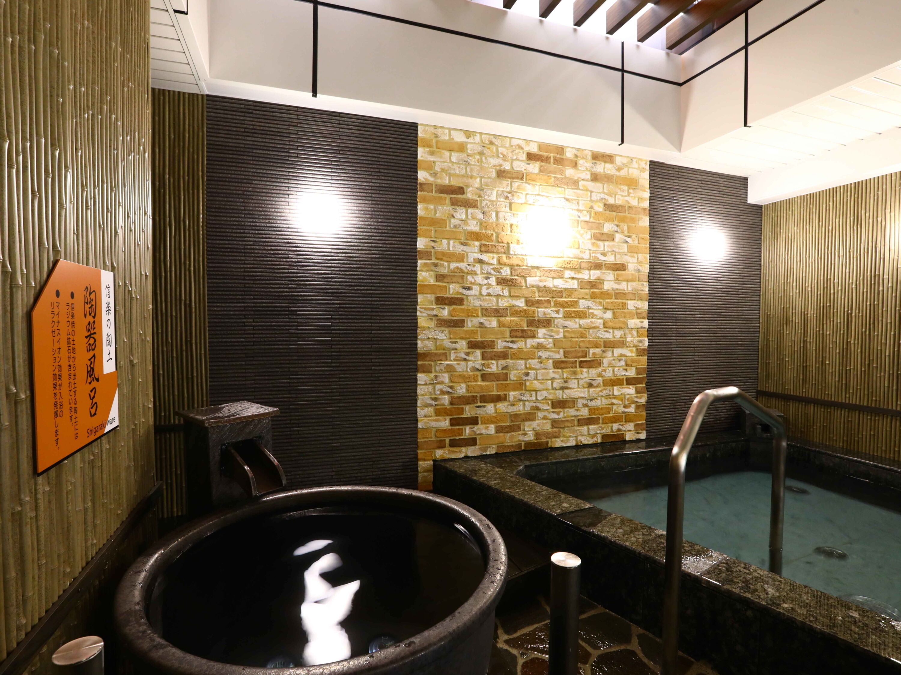 A traditional Japanese onsen with a stone hot spring, a wooden bench, and a bamboo wall.