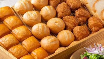 A wooden basket filled with various types of bread, including baguettes and croissants, alongside a bowl of salad.