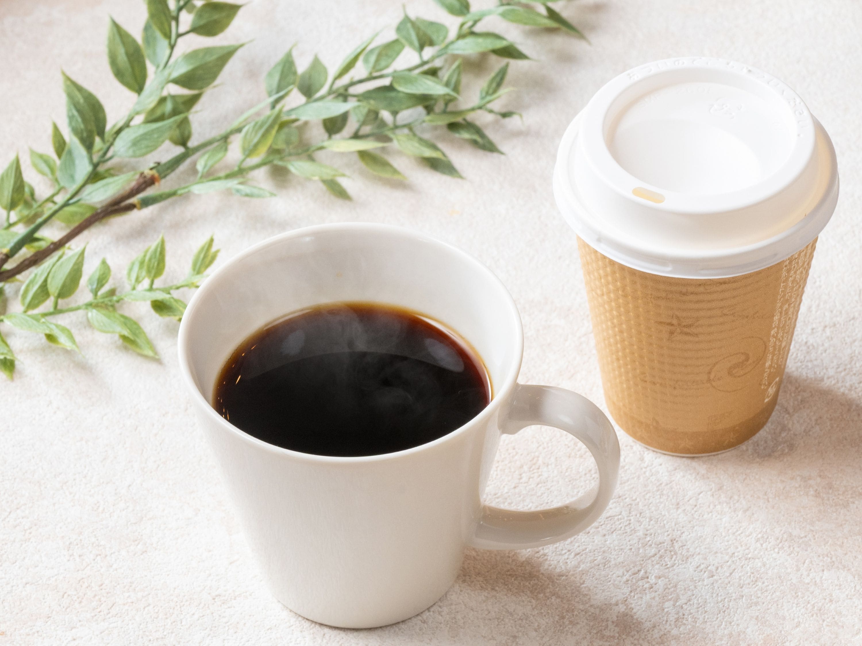 A white ceramic cup filled with a dark liquid, likely coffee, next to a disposable coffee cup with a lid.