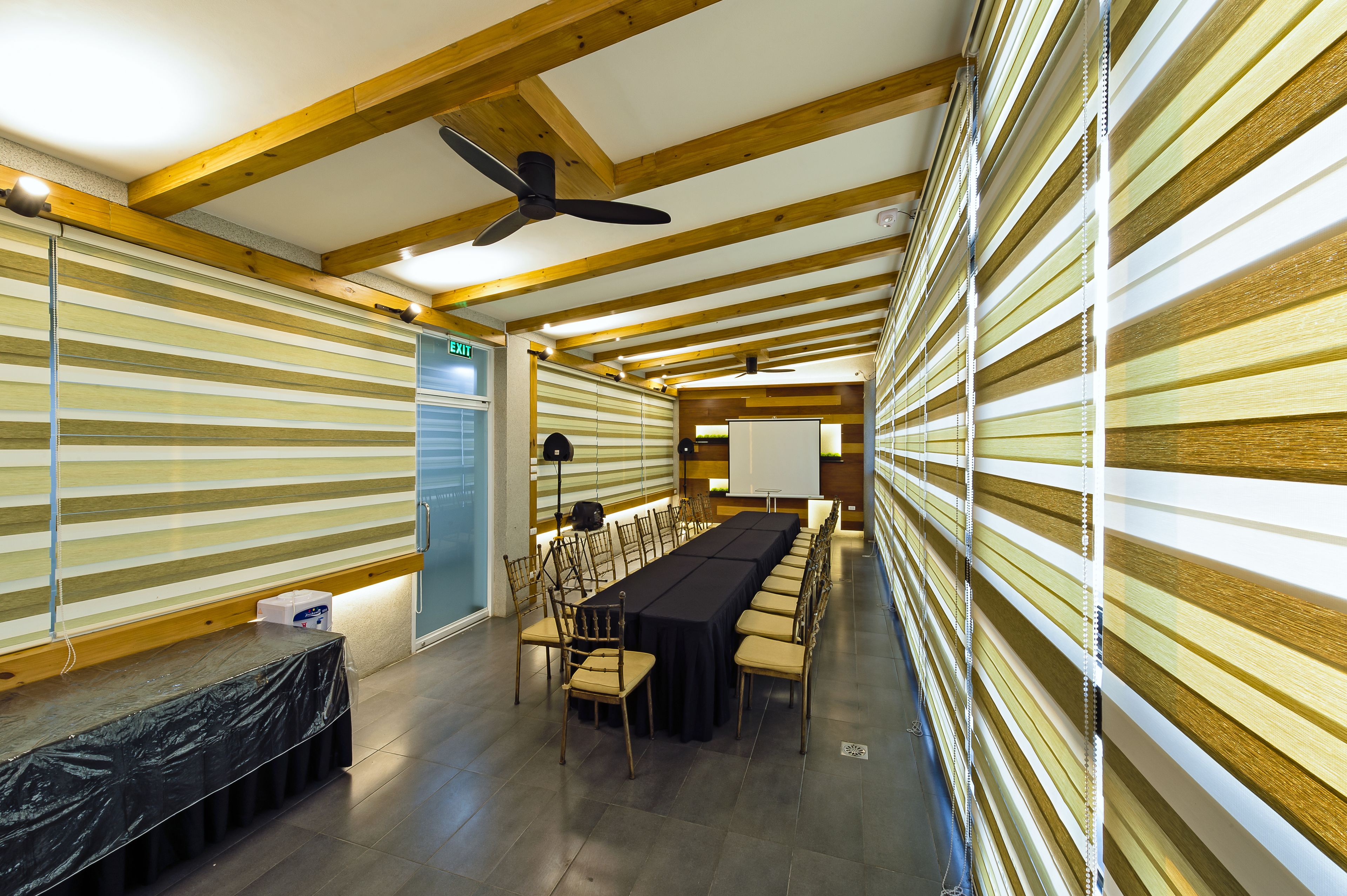 Uma sala de conferências com uma mesa comprida, cadeiras, um ventilador de teto e vigas de madeira.
