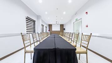 Un salón de conferencias con una mesa larga, sillas, una pantalla de proyector y una puerta con letrero de salida.