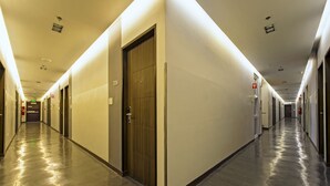 A long, well-lit hallway with multiple doors, each leading to a room. The floor is shiny and reflective, and the walls are plain with a few signs. - Eighty Eight Hotel (Koronadal)