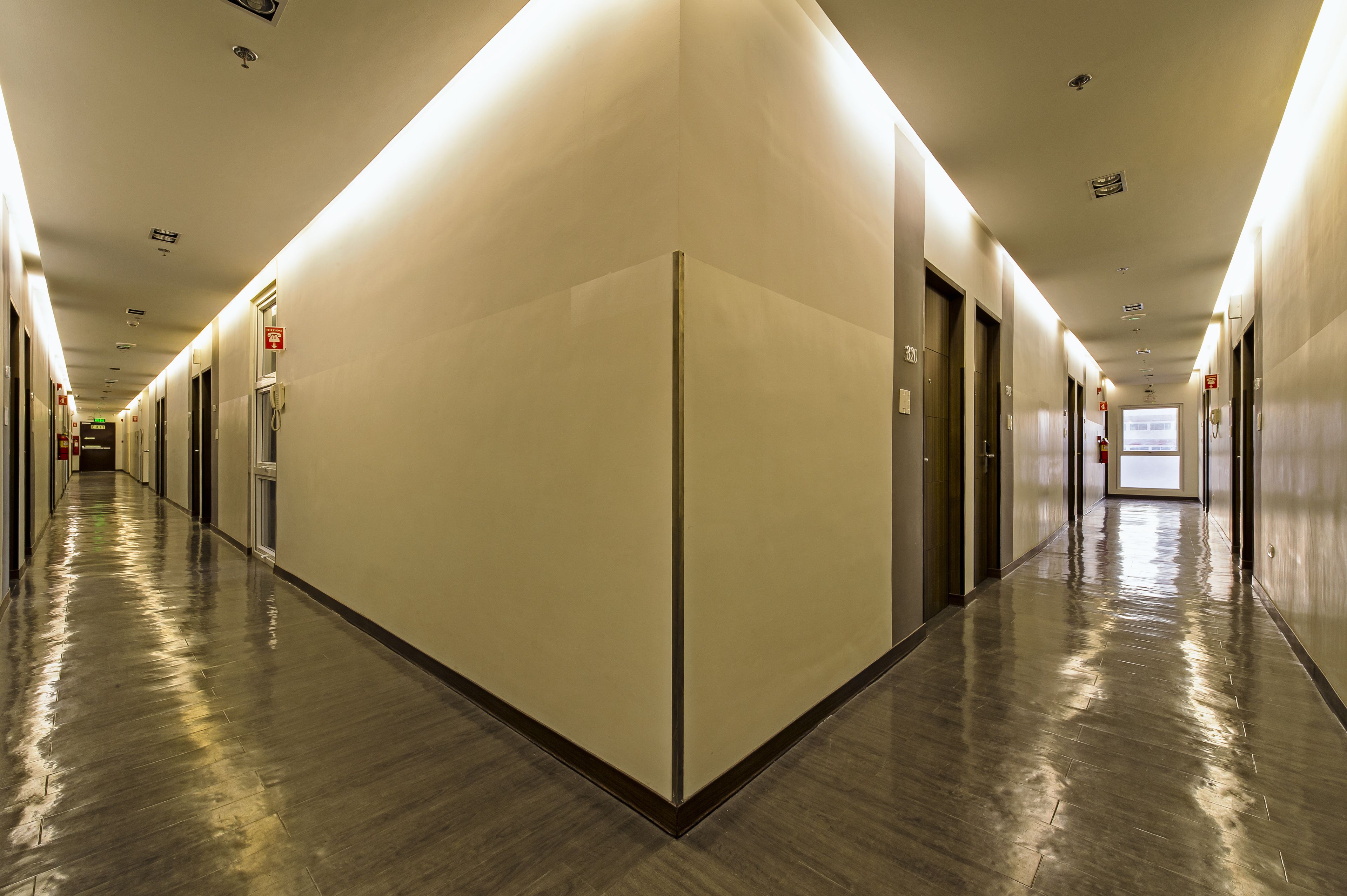 A long, well-lit corridor with doors on both sides, leading to individual rooms.