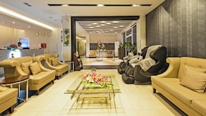A modern hotel lobby with a reception desk, sofas, a massage chair, and a glass coffee table with flowers. - Eighty Eight Hotel (Koronadal)