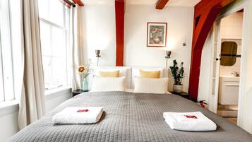 A hotel room with a large bed, two bedside tables, a painting on the wall, and a bathroom visible through an open door.