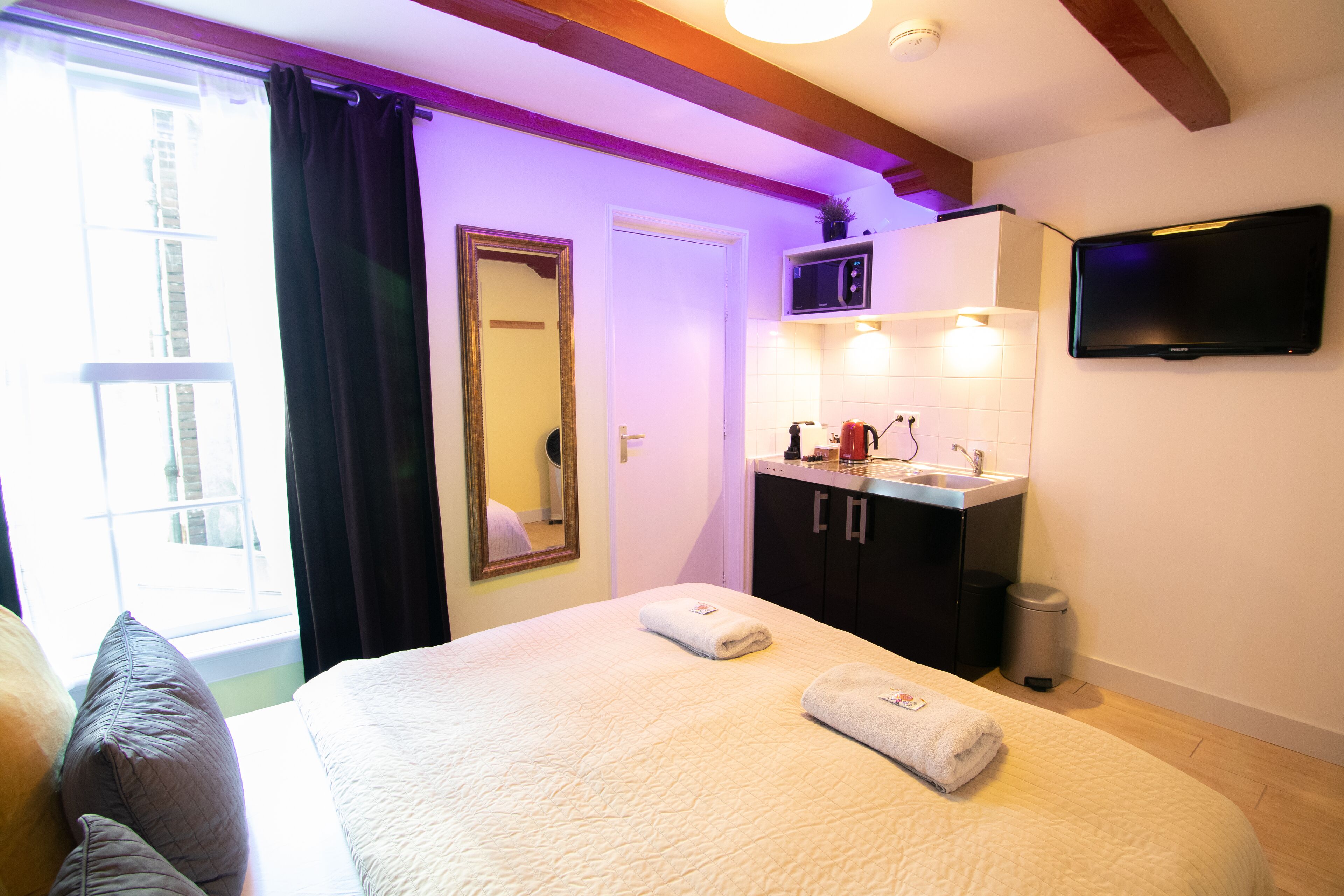Ein Schlafzimmer mit Bett, ein Badezimmer mit Waschbecken und Spiegel sowie ein Fernseher an der Wand.