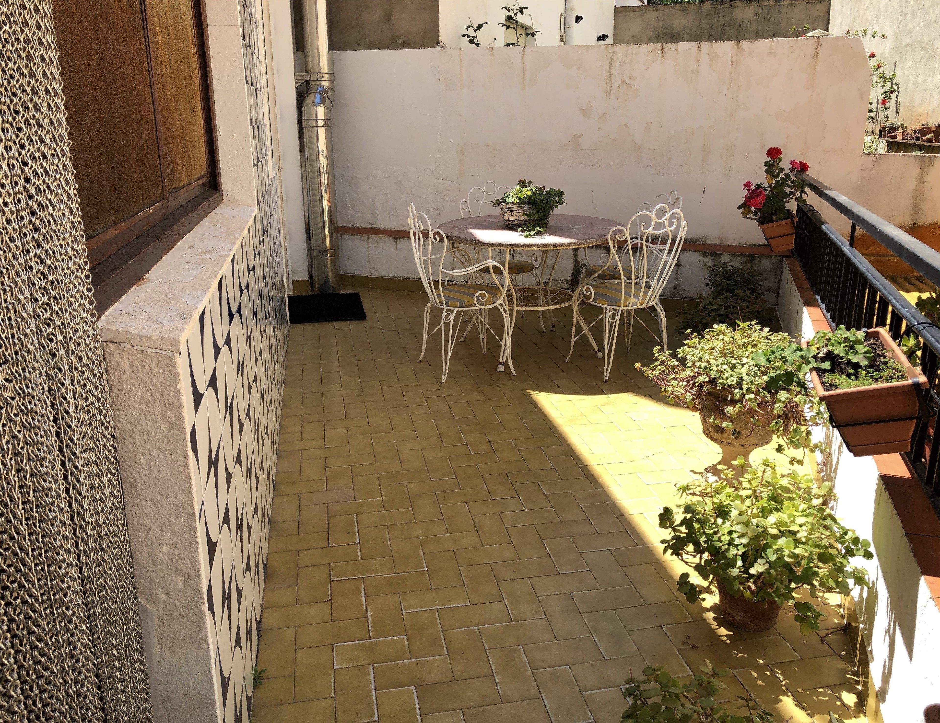 A patio with a tiled floor, a round table with chairs, and potted plants.
