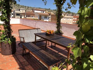 A rooftop terrace with a wooden table and bench, surrounded by potted plants and a basket of fruit. - Casa María (Artana)