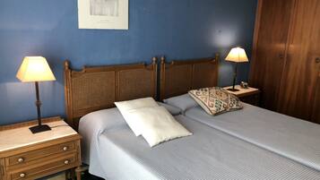 Una cama bien hecha con un cabecero de madera, dos mesitas de noche con lámparas, un armario de madera y una obra de arte enmarcada en la pared.