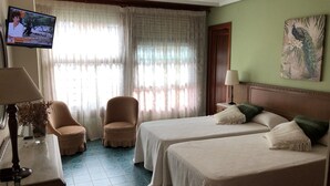 Habitación de hotel con dos camas, televisión, una silla, lámpara y un cuadro en la pared.