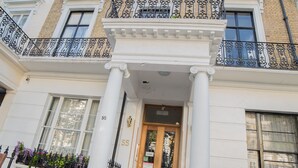 A two-story building with a wooden front door, white columns, and black wrought iron balconies. - New Kent Apartments (London)