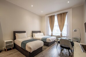 Une chambre d’hôtel avec deux lits, une petite table, une chaise et un bureau avec une lampe.