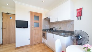 A modern kitchen with wooden cabinets, a built-in oven, a microwave, a granite countertop, a black fan, and a television mounted on the wall. - New Kent Apartments (London)