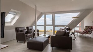 A modern living room with a large window, a sofa, a coffee table, and a patterned chair. - Strandhaus Christiansen (Cuxhaven)