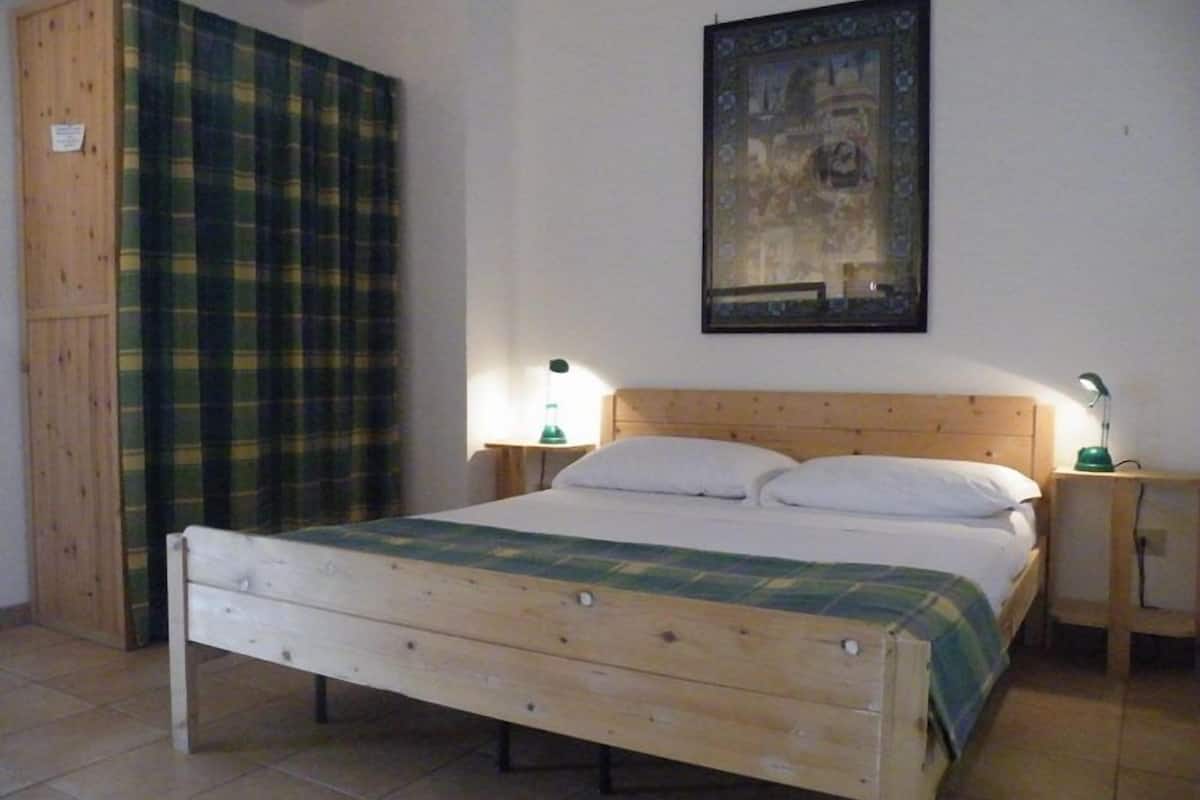 Una camera da letto con un letto di legno, una tenda a quadri, un quadro appeso al muro e due comodini con lampade.