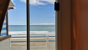 Habitación con un amplio ventanal con vista a una playa y barandilla.
