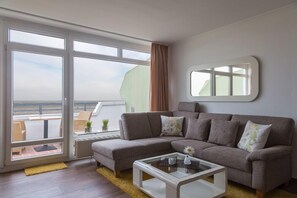 A modern living room with a large window, a sofa, a coffee table, and a small side table. - Panoramahaus Duhnen (Cuxhaven)