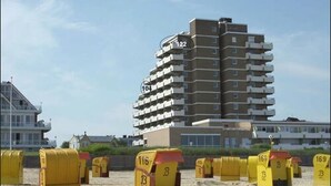 A high-rise building with multiple balconies, numbered 104 and 122, and a beach area with yellow mailboxes labeled with numbers like 116 and 169.