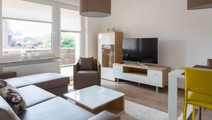 Un salon moderne avec un canapé, une table basse, un téléviseur et un coin repas agrémenté d’une chaise jaune.