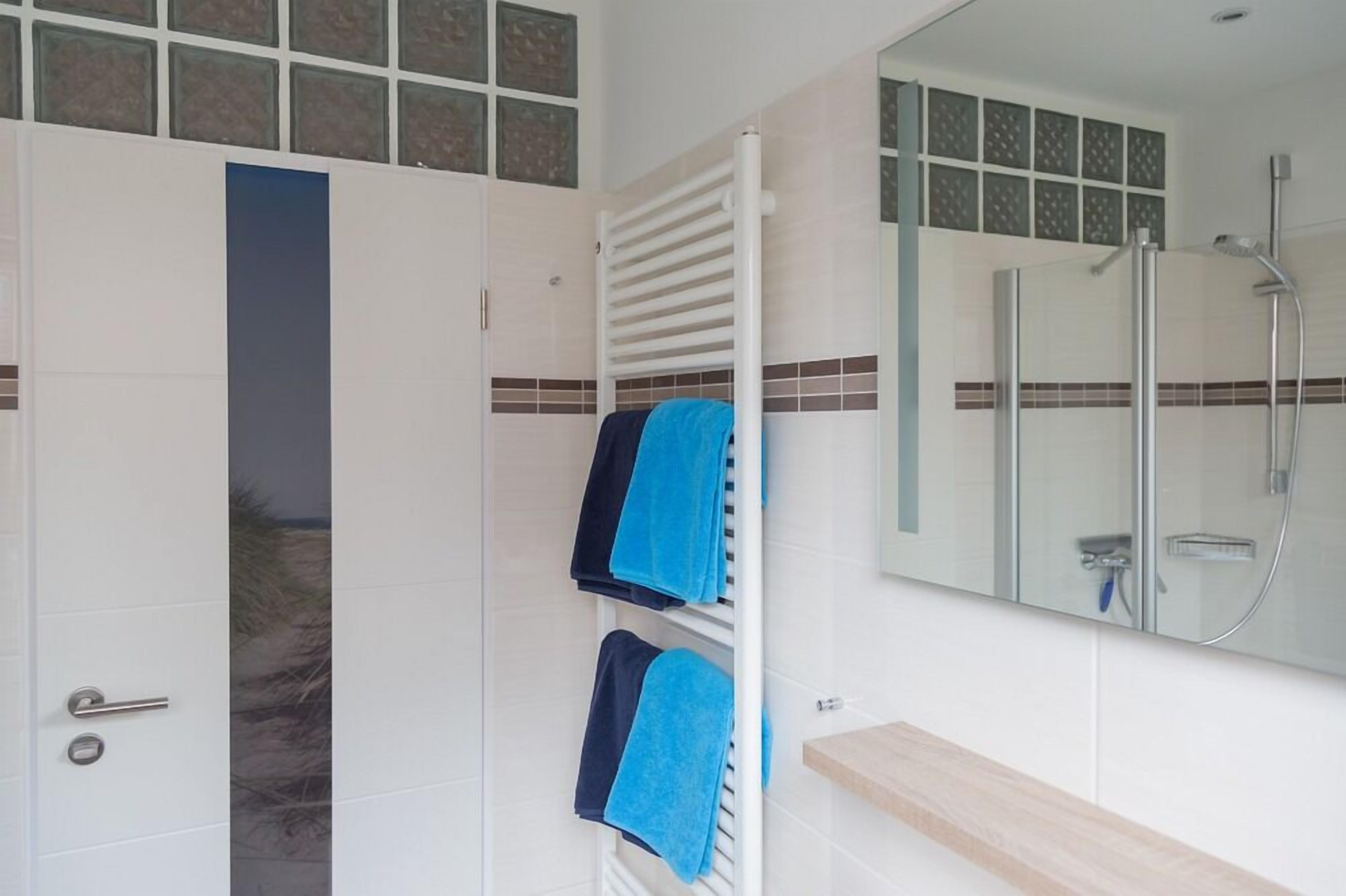 Casa de banho com cabine de duche em vidro, um porta-toalhas com toalhas azuis e uma porta branca com uma faixa vertical azul.