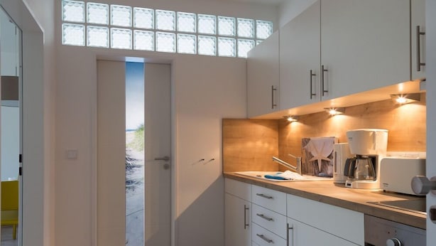 Une cuisine moderne avec des meubles blancs, un plan de travail en bois et une machine à café.
