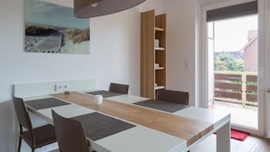 Un espace repas moderne avec une longue table, des chaises et un luminaire suspendu.