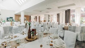 Un amplio salón de banquetes con mesas redondas dispuestas para un evento formal, ventanas grandes y un techo alto.
