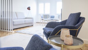 Uma sala de estar moderna com um sofá cinza, uma poltrona azul e uma mesa de centro com vasos decorativos.