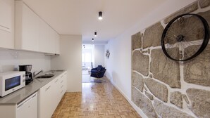 Uma cozinha moderna com armários brancos, micro-ondas e pia. Há uma parede de pedra com relógio e um chão de madeira em padrão herringbone.