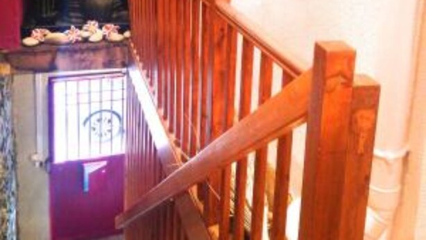 A staircase with wooden railings, a red door at the bottom, and a potted plant on the wall. - Le Petit Blanzou (Pierre-Buffiere)