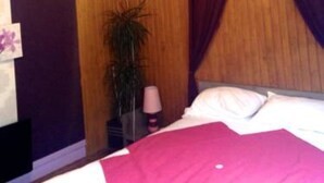A bedroom with a bed, a nightstand, a lamp, and a potted plant. - Le Petit Blanzou (Pierre-Buffiere)