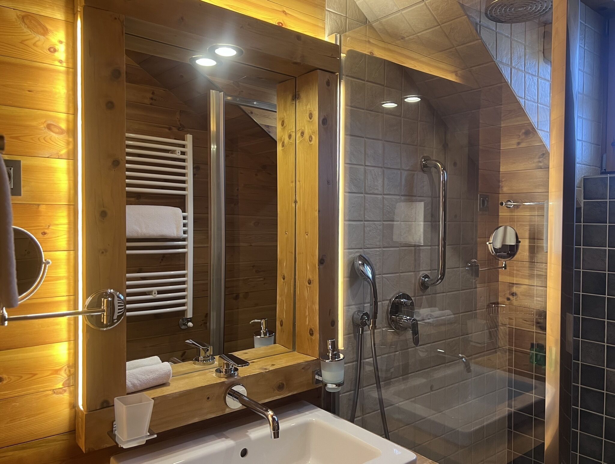 Un baño moderno con interiores de madera, cabina de ducha acristalada y lavamanos con espejo y toallero.