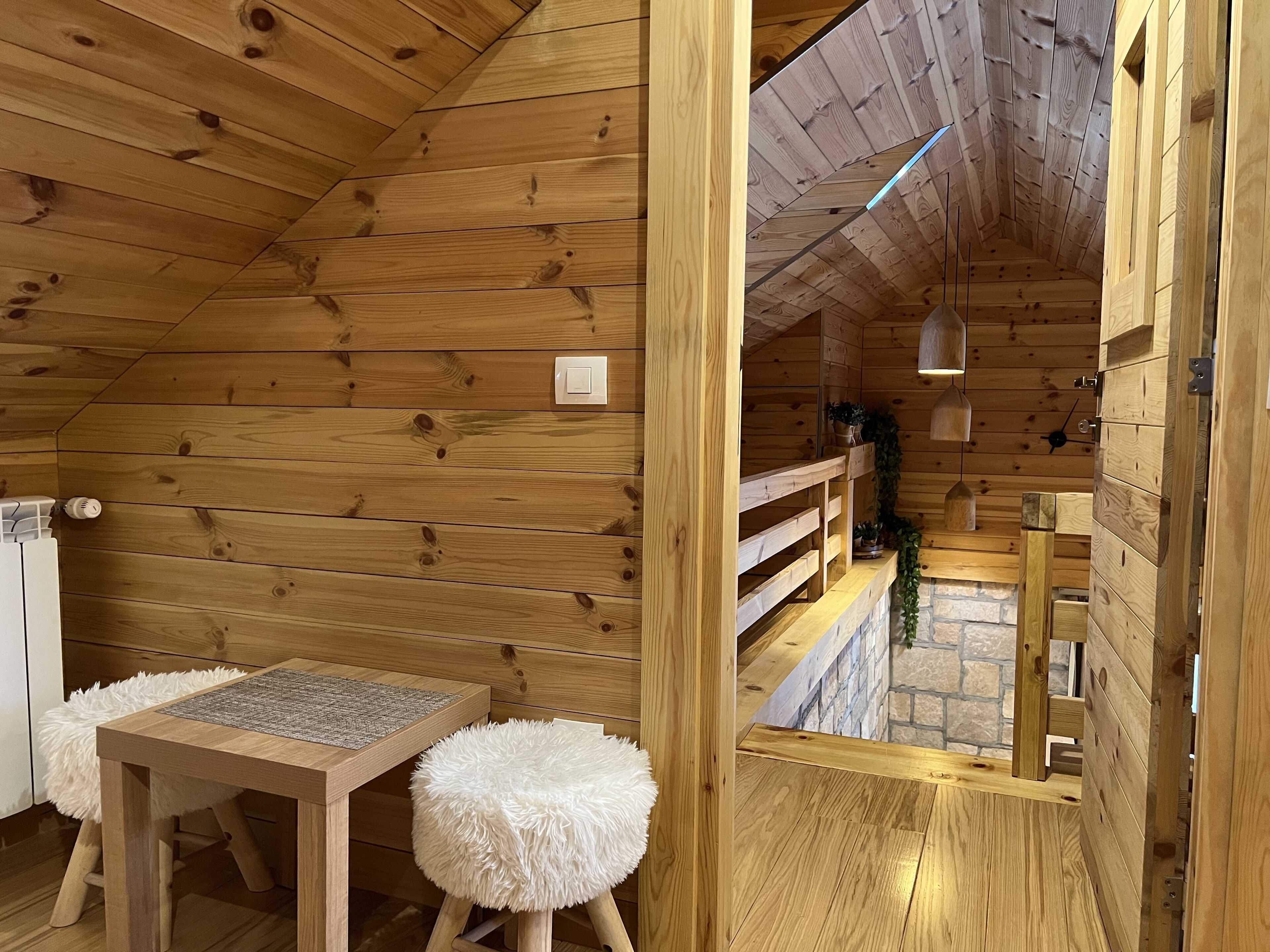 A wooden interior with a table and stool, a small window, and a stone wall.