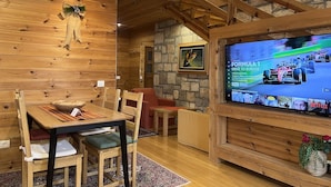 A cozy wooden cabin interior with a dining area, a television displaying a Formula 1 race, and a stone wall. - Chalet Kolasin Montenegro (Kolašin)