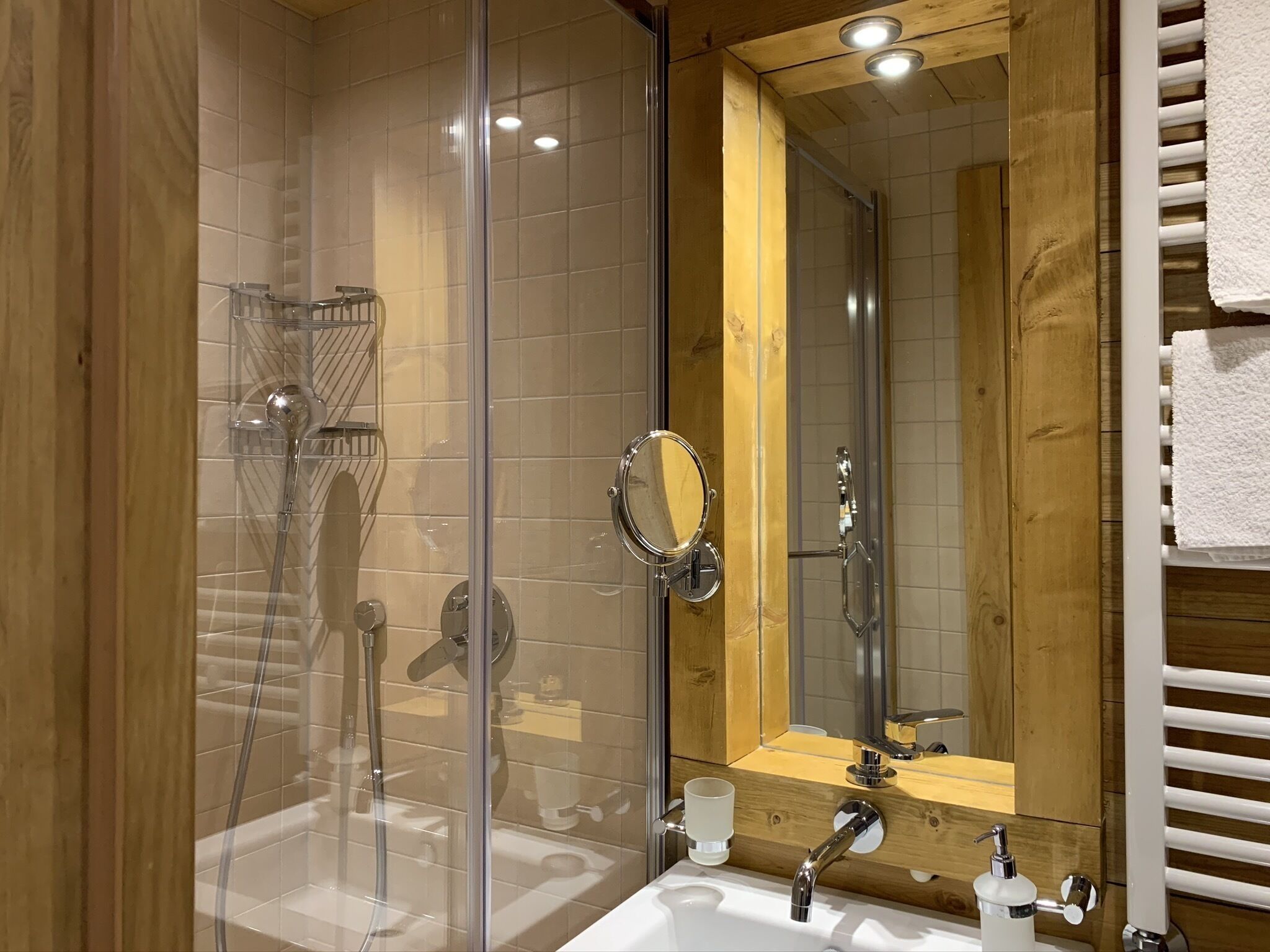 Une salle de bain moderne dotée d’une douche en verre, d’un meuble-lavabo en bois avec un miroir et d’un lavabo blanc avec un distributeur de savon.