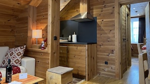 A cozy cabin interior with wooden walls, a kitchenette, a sofa with patterned cushions, and a small table with a bottle and papers. - Chalet Kolasin Montenegro (Kolašin)