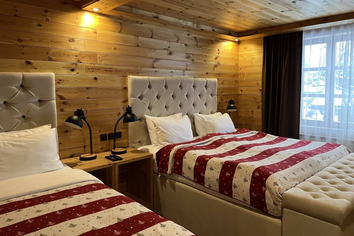 Une chambre d’hôtel avec des murs lambrissés, deux lits dotés de têtes de lit capitonnées, des lampes de chevet et une fenêtre avec des rideaux.
