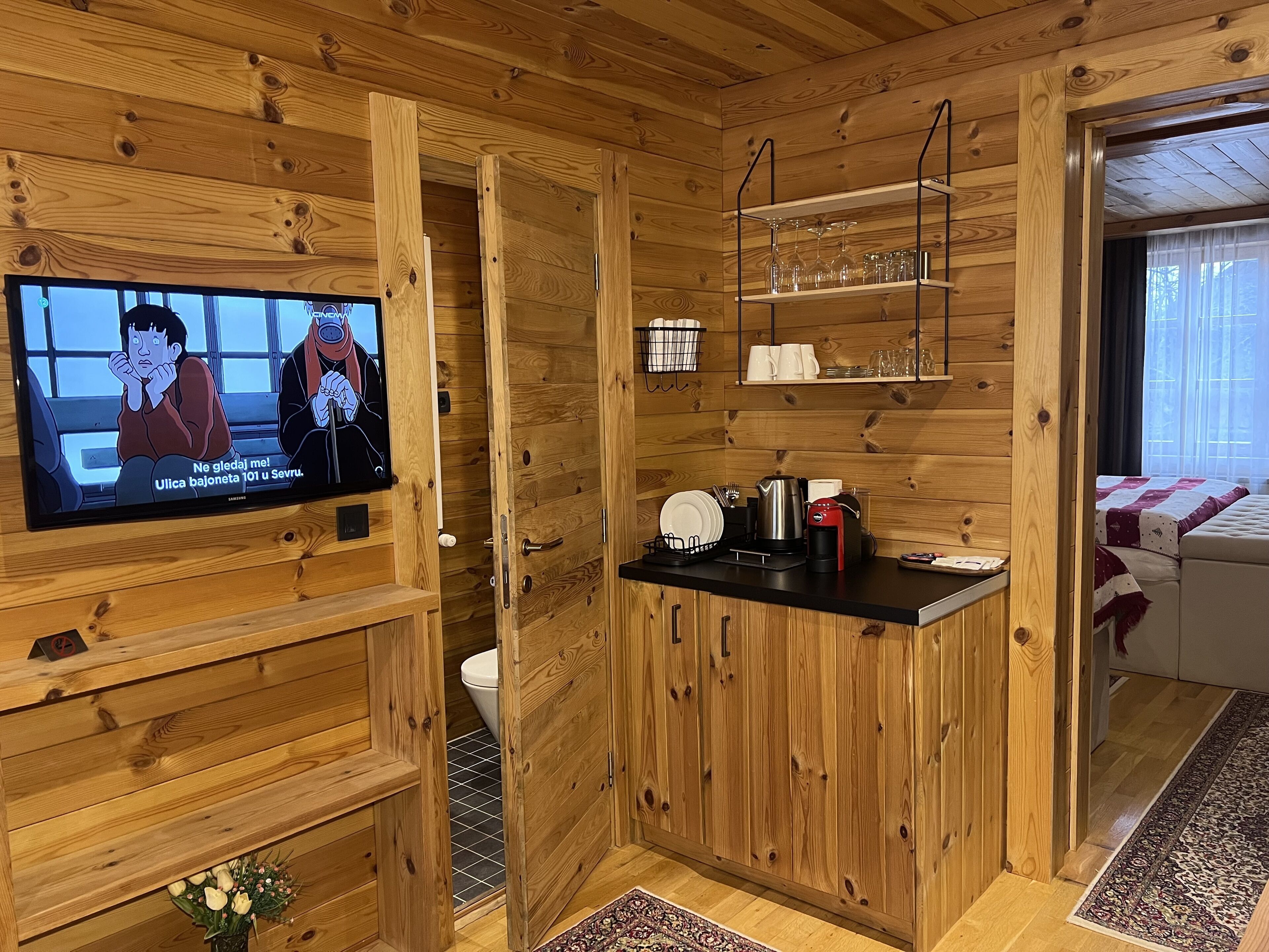 A wooden cabin interior with a TV, wooden shelves, a coffee maker, and a small kitchen area.