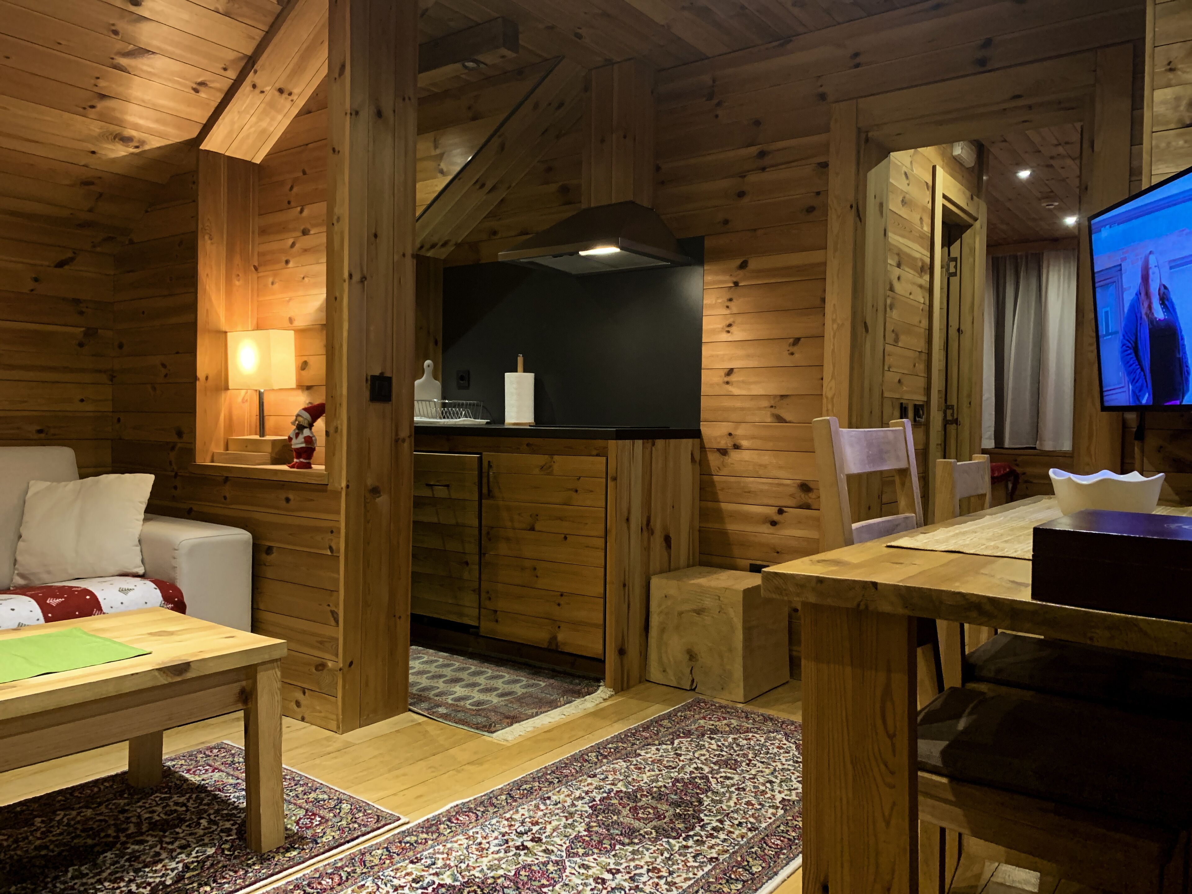Interior acollidor d'una cabana de fusta amb zona de menjador, sofà, televisió i cuina.