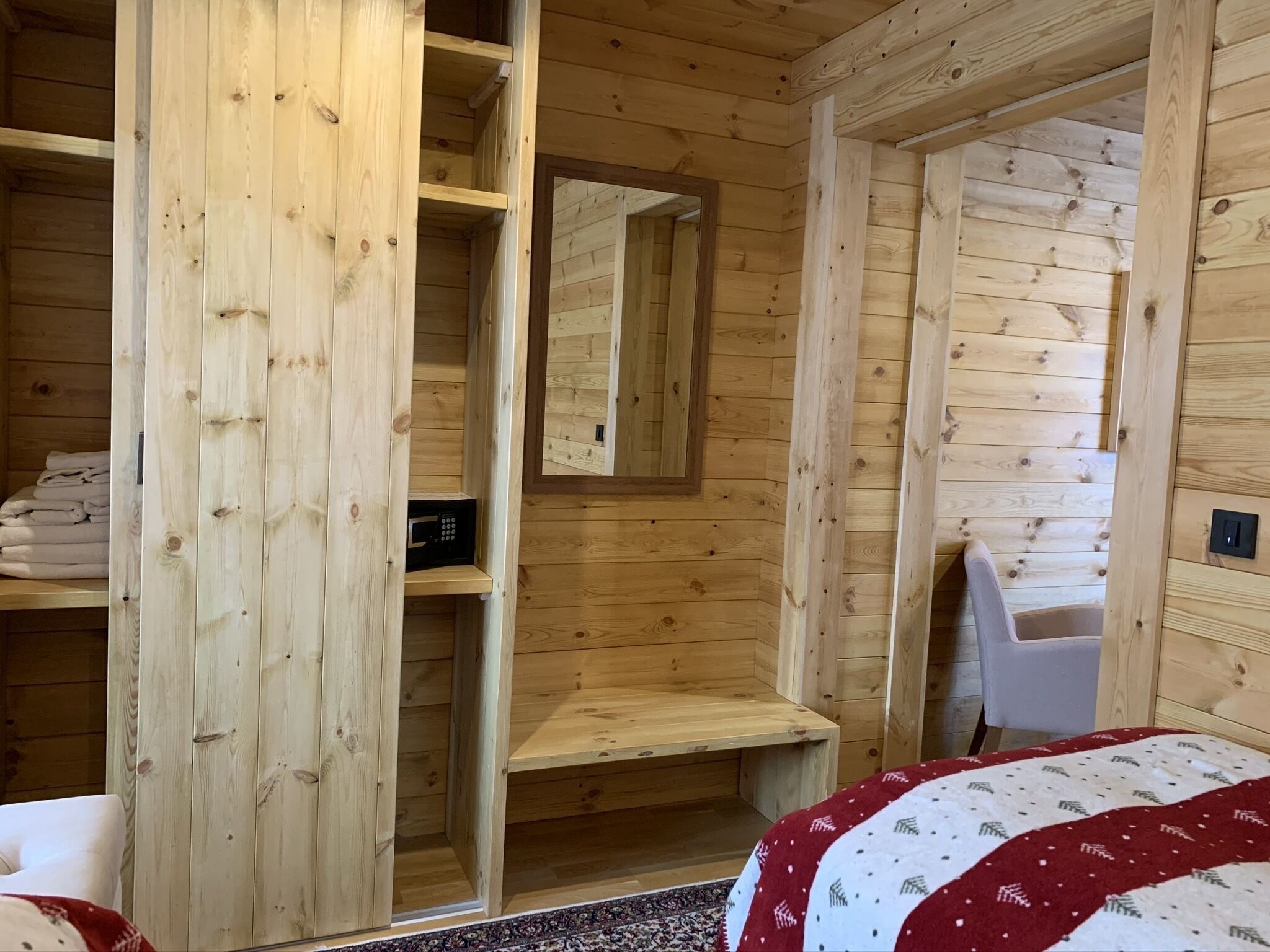 Puisesta hirrestä rakennettu mökki, jossa on sänky, penkki ja peili.