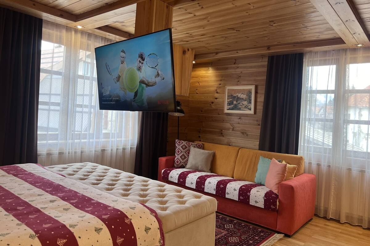 Une pièce confortable avec un grand lit, un canapé rouge et un téléviseur diffusant un événement de tennis.