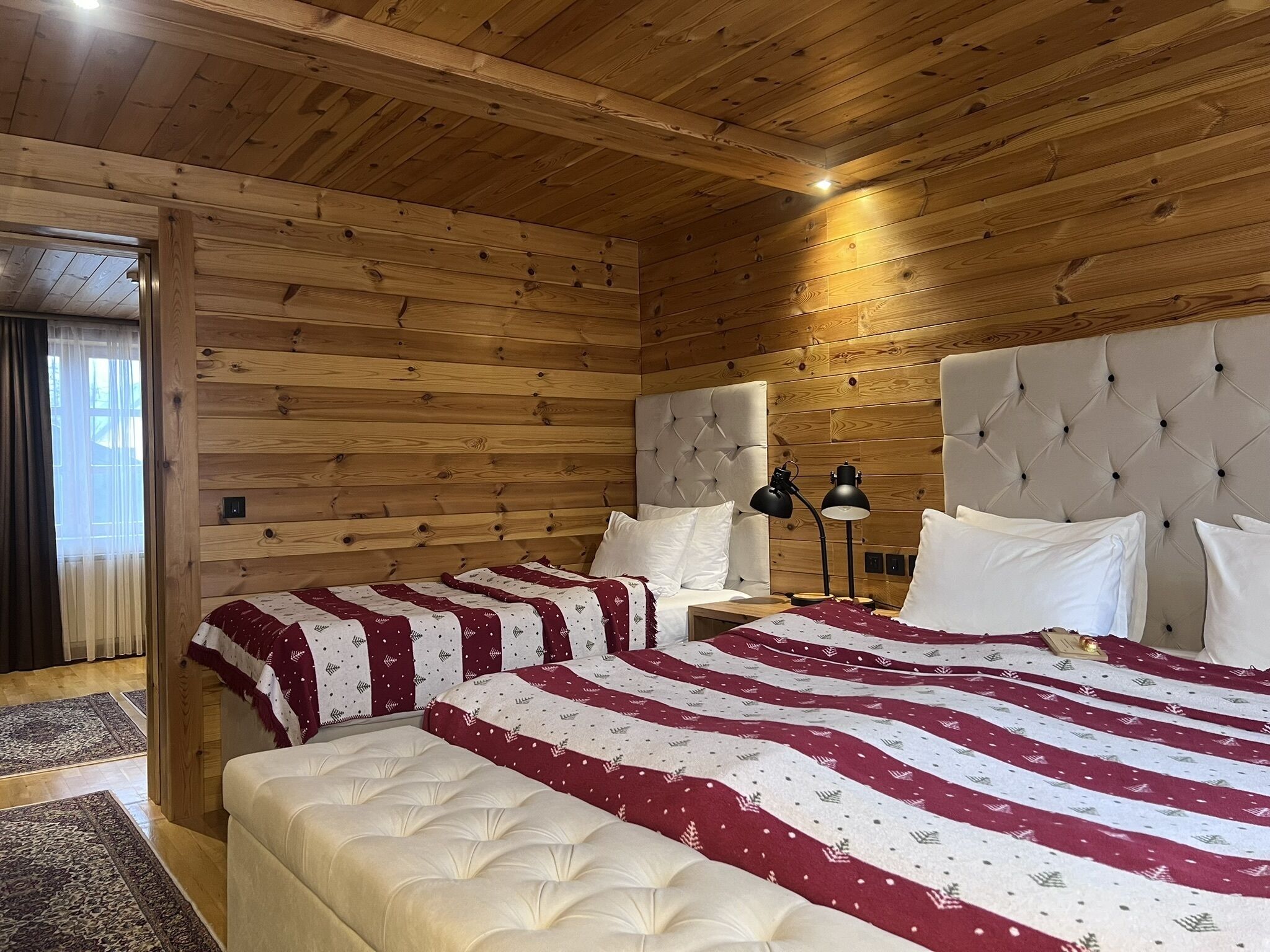 Un dormitorio con paneles de madera, dos camas, cabeceros acolchados y una mesita de noche con lámpara.