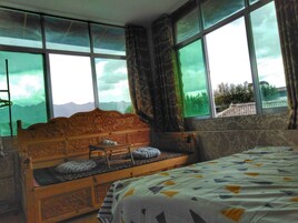 Un dormitorio con cama de madera, una ventana con vista a las montañas y una colcha estampada.