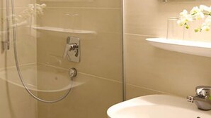 Un baño moderno con ducha envuelta en vidrio, lavamanos pedestal y espejo sobre él.
