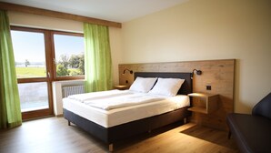 Un dormitorio con una cama grande, cabecera de madera, mesita de noche, una banca y vista a un campo verde a través de una ventana.
