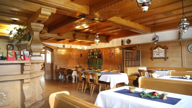 Restaurante con vigas de madera, candelabros y decoración tradicional. Las mesas están dispuestas con manteles blancos y sillas de madera.