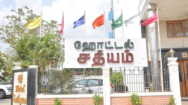 A hotel sign with multiple flags and a gated entrance. - Hotel Sathyam (Pudukkottai)