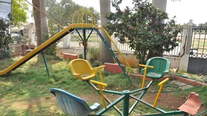 A playground with a swing set, a slide, and a climbing structure. - Hotel Sathyam (Pudukkottai)