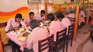 A group of people dining at a restaurant with a table set for a meal, chairs, and a decorative wall. - Hotel Sathyam (Pudukkottai)